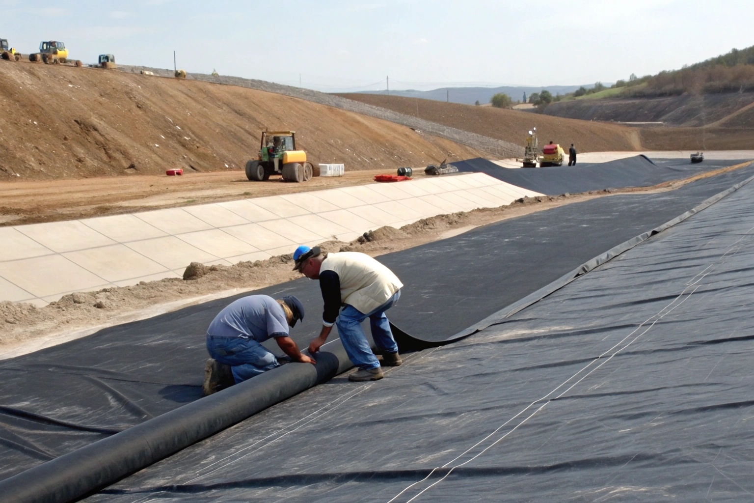 An inspector reviewing a geomembrane's Technical Data Sheet with a roll of the material in the background