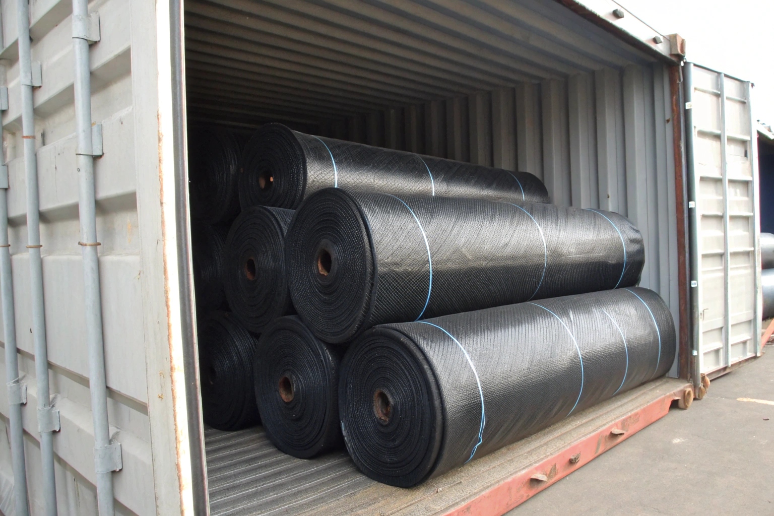 A close-up of a properly packaged geomembrane roll wrapped in black woven geotextile with secure straps
