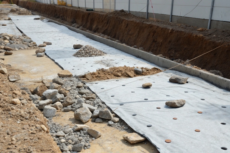 A close-up photo of a geomembrane liner punctured by a sharp rock from underneath