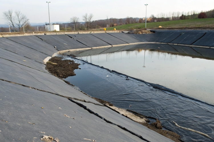 A contractor inspecting a geomembrane liner with a tear