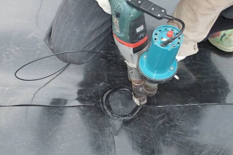 A technician using a handheld extrusion welder to create a seal around a pipe boot