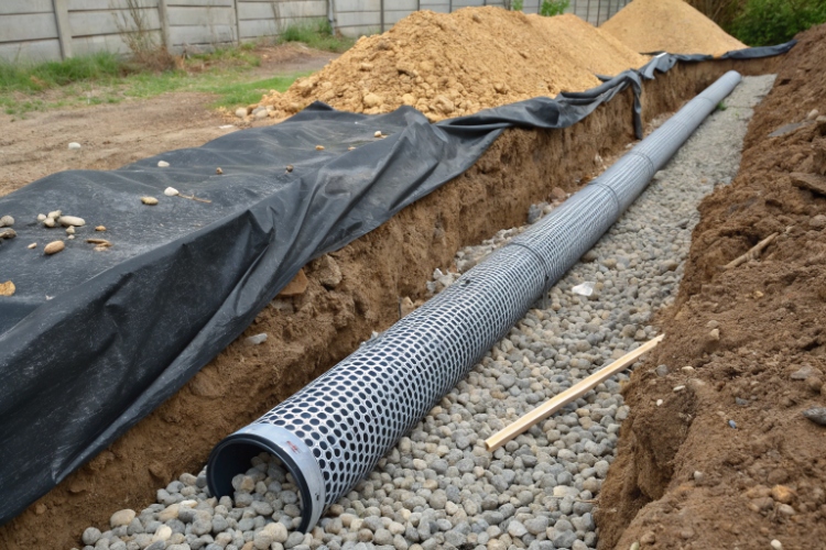 A construction photo showing workers installing a French drain by wrapping a perforated pipe and gravel in nonwoven geotextile fabric