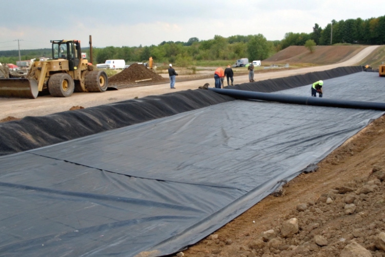 A cross-section diagram of a road showing a geomembrane layer separating the subgrade from the aggregate base