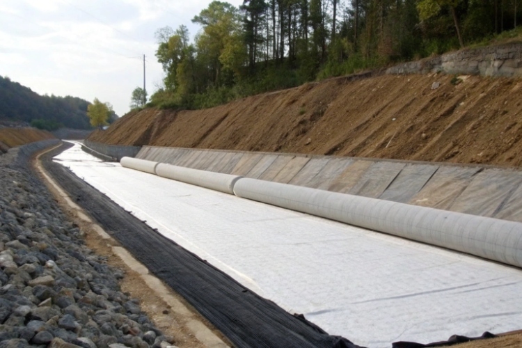 A photo of a road construction site showing a layer of white nonwoven geotextile separating soil and gravel layers