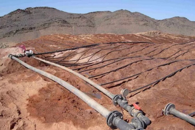 An expansive aerial view of a large-scale heap leach pad in a mountain landscape, showing its massive footprint.
