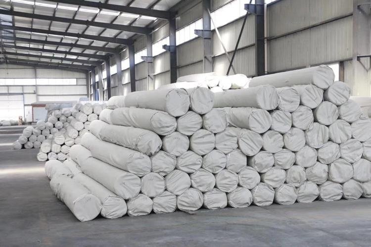 Neatly stacked GCL rolls on dunnage and covered with a waterproof tarp at a construction site.