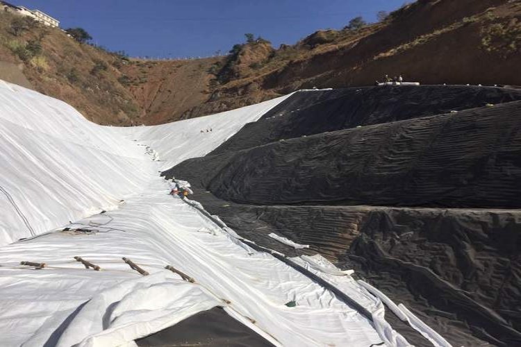 A team of workers installing a black HDPE geomembrane liner on a prepared slope