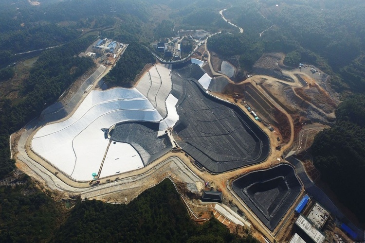 An aerial view of a large new landfill cell with geomembrane being installed on the slopes and base