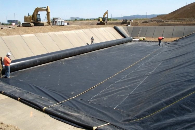 A close-up shot of a thick, nonwoven geotextile being laid over a geomembrane as a protective cushion layer.