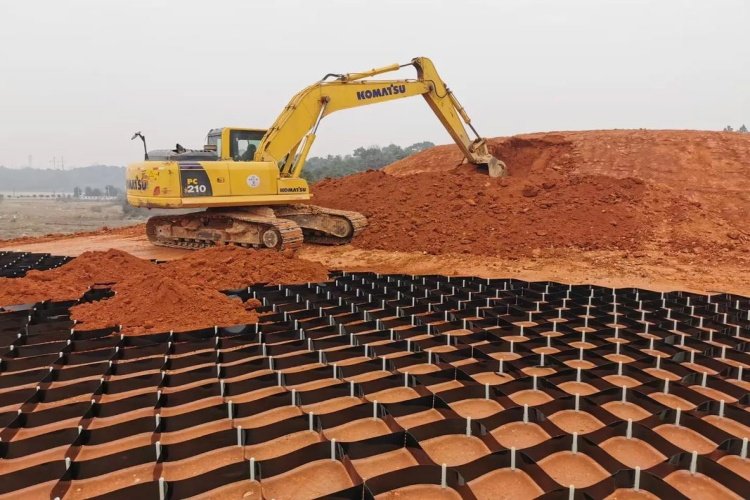 A front loader carefully placing gravel infill into the expanded geocell structure