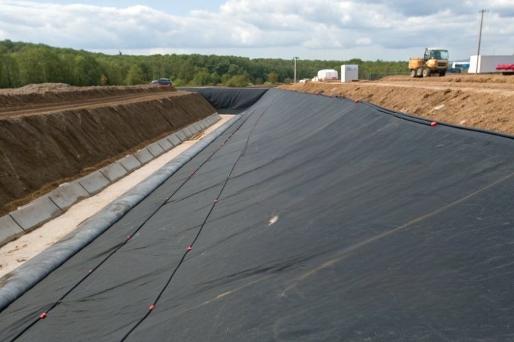 A large roll of black HDPE geomembrane waiting to be unrolled and installed at a mining site.