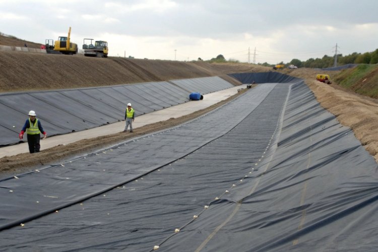 A wide-angle shot of a large landfill cell with geomembrane panels being installed on a steep slope, showing clear seaming lines.