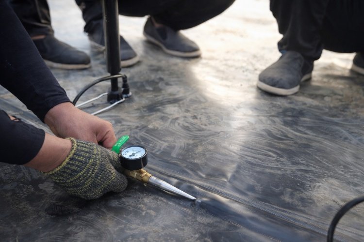 Close-up of a dual-track fusion weld on a black geomembrane liner with air pressure testing equipment