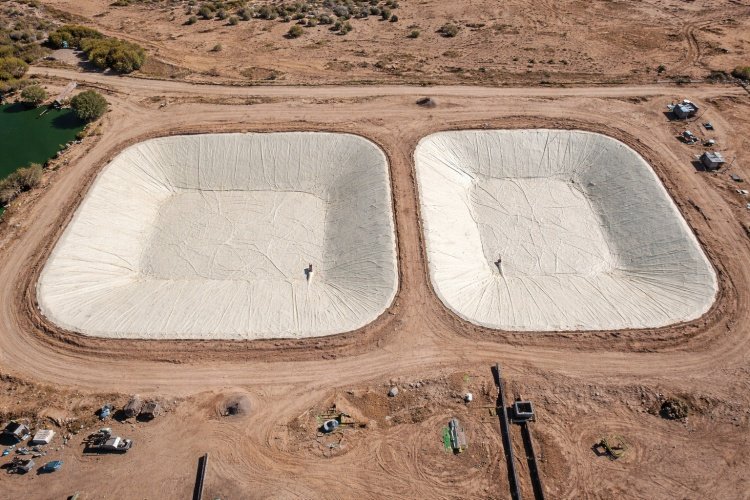 A construction crew carefully deploying large panels of black HDPE geomembrane to line an excavated anaerobic lagoon.