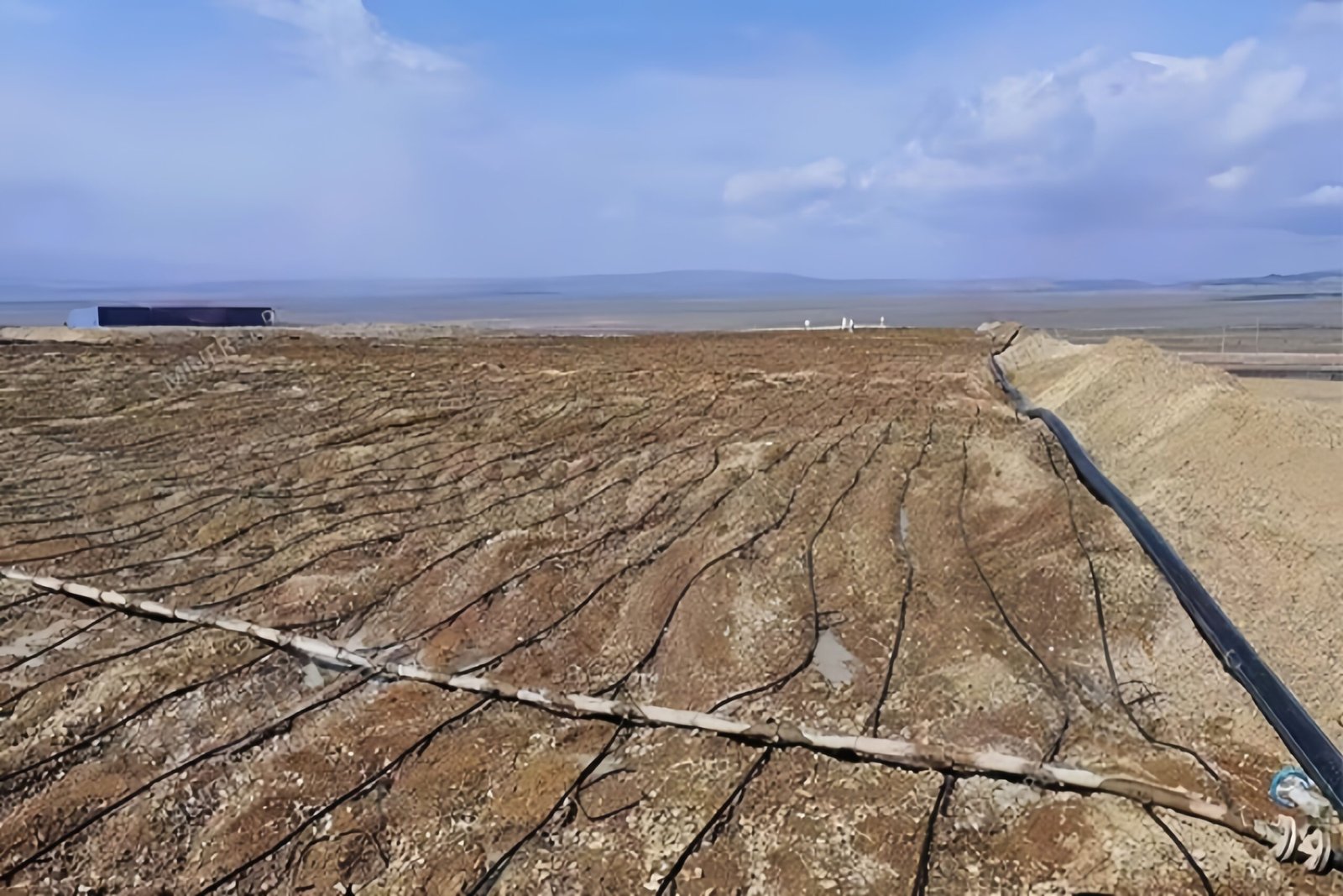 An aerial view of an active heap leach pad with trucks and stacking equipment placing ore on the lined surface.